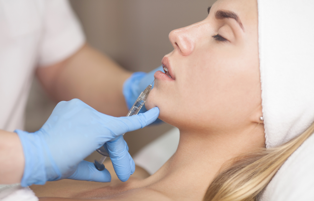 The cosmetologist makes injections of botulinum toxin in the lips of the patient.
