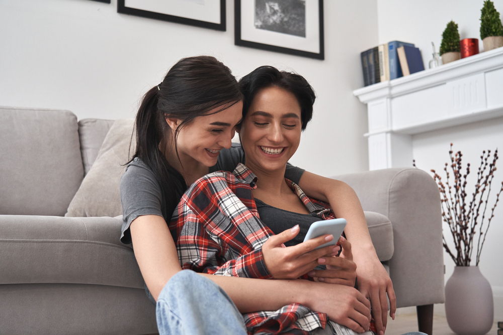 Young Happy Lesbian Lgbtq Couple Or Friends Holding Smartphone Using