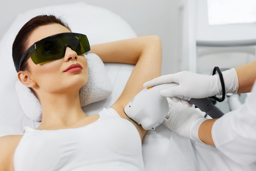 A woman laying down with goggles on getting Laser Hair Removal on her underarms